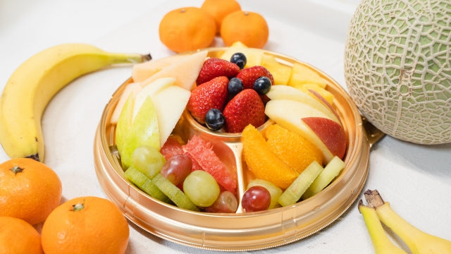 Platter of sliced fruit including apples, bananas, grapes, oranges, and melon.