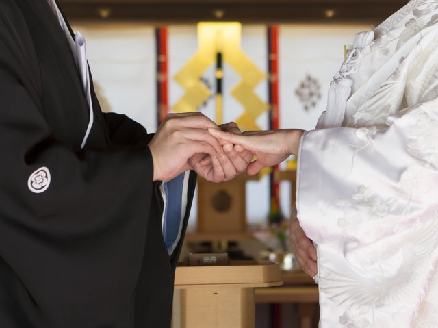 A couple wearing traditional Japanese wedding attire exchange rings during a wedding ceremony.
