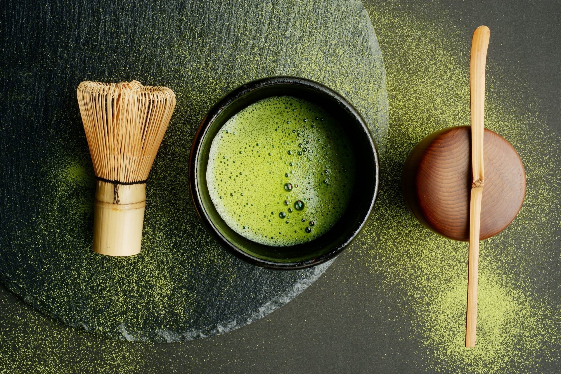 Matcha and matcha tools, including a chasen (matcha whisk) against a black background